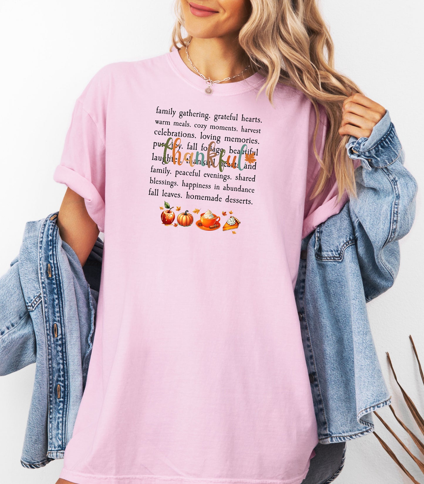 Person wearing a Blossom soft pink T-shirt with a festive “Thankful” harvest-themed design featuring fall words like family gathering, grateful hearts, cozy moments, and homemade desserts, with autumn illustrations of an apple, pumpkin, pie, and fall leaves. A warm and cheerful tee perfect for Thanksgiving, family gatherings, or celebrating the fall season.
