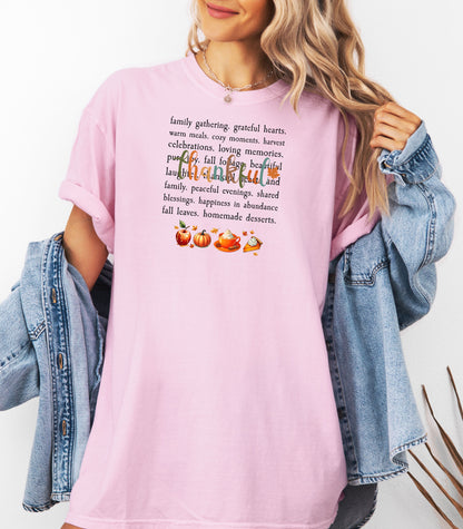 Person wearing a Blossom soft pink T-shirt with a festive “Thankful” harvest-themed design featuring fall words like family gathering, grateful hearts, cozy moments, and homemade desserts, with autumn illustrations of an apple, pumpkin, pie, and fall leaves. A warm and cheerful tee perfect for Thanksgiving, family gatherings, or celebrating the fall season.