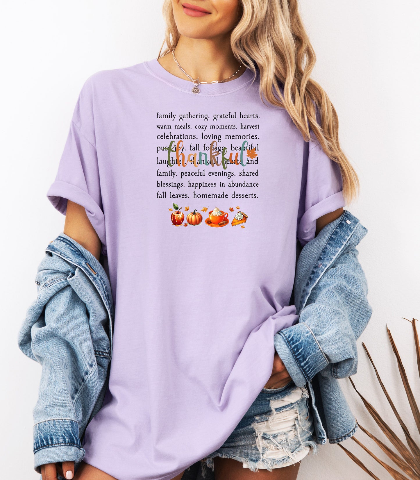 Person wearing an Orchid T-shirt with a festive “Thankful” harvest-themed design featuring fall words like family gathering, grateful hearts, cozy moments, and homemade desserts, with autumn illustrations of an apple, pumpkin, pie, and fall leaves. A warm and cheerful tee perfect for Thanksgiving, family gatherings, or celebrating the fall season.