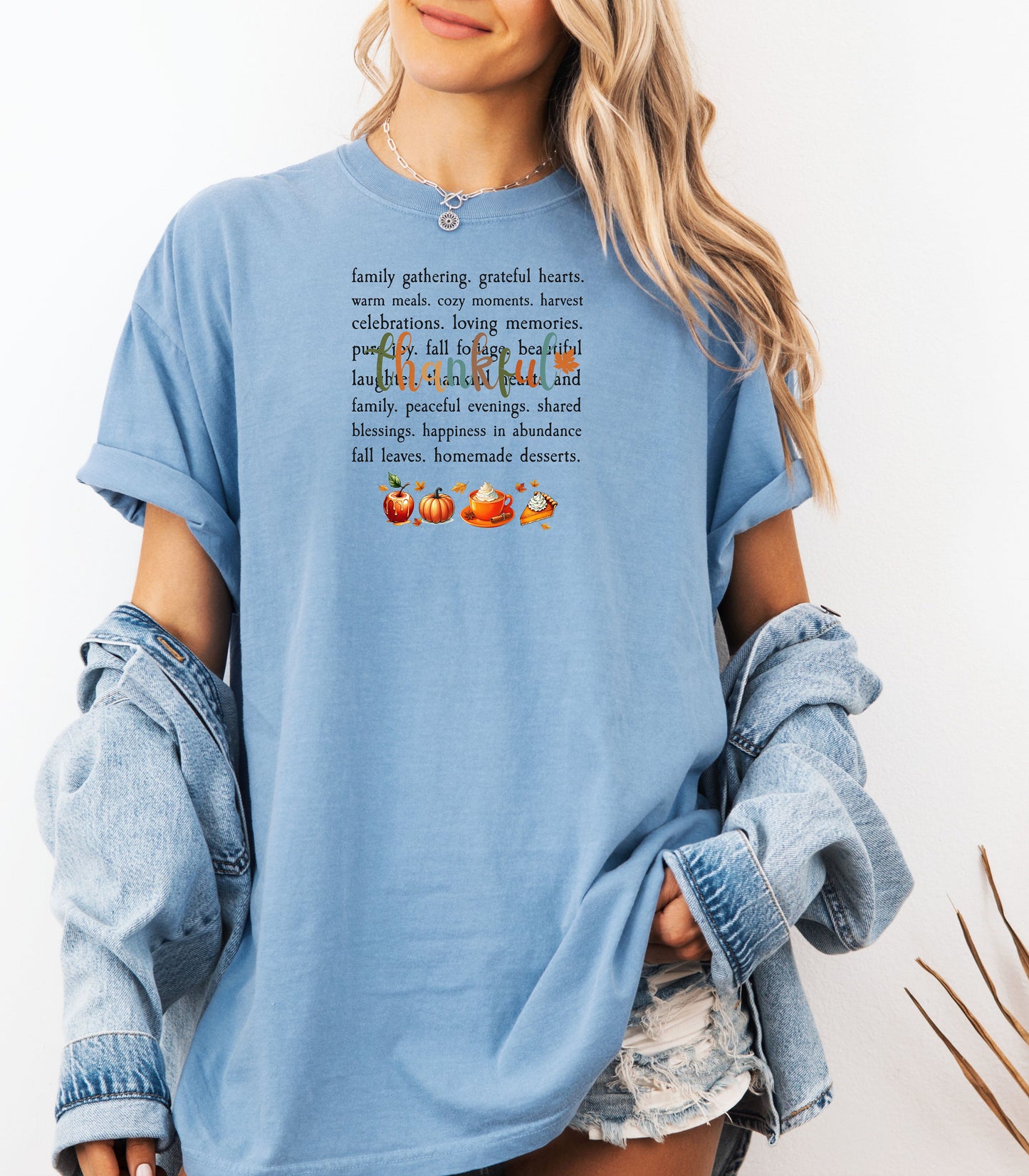 Person wearing a Washed Denim T-shirt with a festive “Thankful” harvest-themed design featuring fall words like family gathering, grateful hearts, cozy moments, and homemade desserts, with autumn illustrations of an apple, pumpkin, pie, and fall leaves. A warm and cheerful tee perfect for Thanksgiving, family gatherings, or celebrating the fall season.
