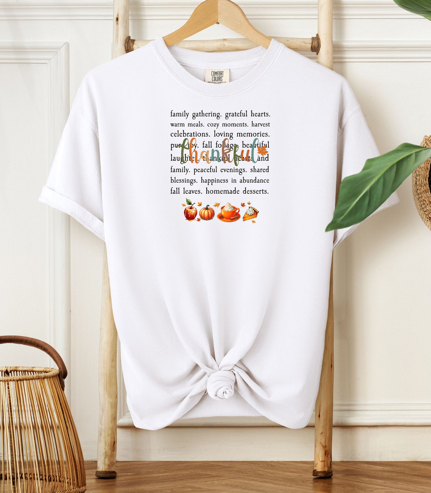 A White T-shirt with a festive “Thankful” harvest-themed design featuring fall words like family gathering, grateful hearts, cozy moments, and homemade desserts, with autumn illustrations of an apple, pumpkin, pie, and fall leaves. A warm and cheerful tee perfect for Thanksgiving, family gatherings, or celebrating the fall season.