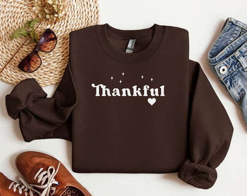Dark Chocolate Gildan sweatshirt featuring the word “Thankful” in bold white retro-style font, accented with small sparkling stars above and a heart below. A simple yet meaningful design that celebrates gratitude and cozy fall vibes—perfect for Thanksgiving, autumn gatherings, or everyday wear.
