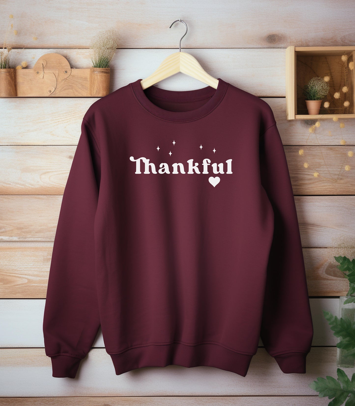 Maroon Gildan sweatshirt featuring the word “Thankful” in bold white retro-style font, accented with small sparkling stars above and a heart below. A simple yet meaningful design that celebrates gratitude and cozy fall vibes—perfect for Thanksgiving, autumn gatherings, or everyday wear.