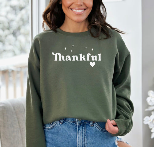 Military Green Gildan sweatshirt featuring the word “Thankful” in bold white retro-style font, accented with small sparkling stars above and a heart below. A simple yet meaningful design that celebrates gratitude and cozy fall vibes—perfect for Thanksgiving, autumn gatherings, or everyday wear.