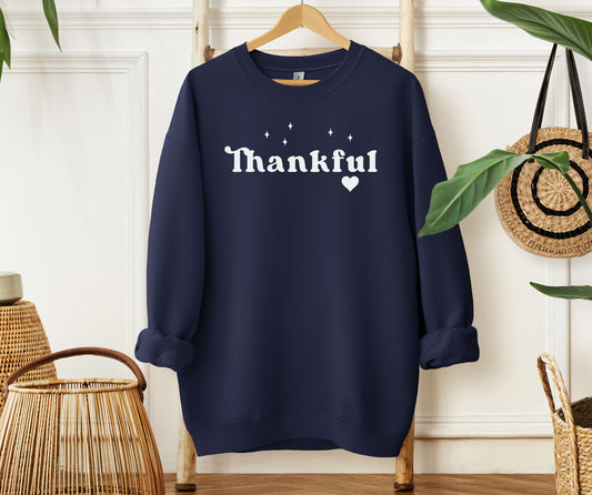 Navy Gildan sweatshirt featuring the word “Thankful” in bold white retro-style font, accented with small sparkling stars above and a heart below. A simple yet meaningful design that celebrates gratitude and cozy fall vibes—perfect for Thanksgiving, autumn gatherings, or everyday wear.