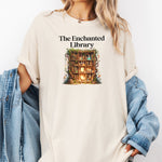 Woman wearing an Ivory t-shirt featuring a magical design titled "The Enchanted Library." The graphic shows a glowing bookshelf framed by vines, candles, books, and potions, evoking a whimsical, fantasy-inspired library setting. Perfect for book lovers and fans of enchanted tales.