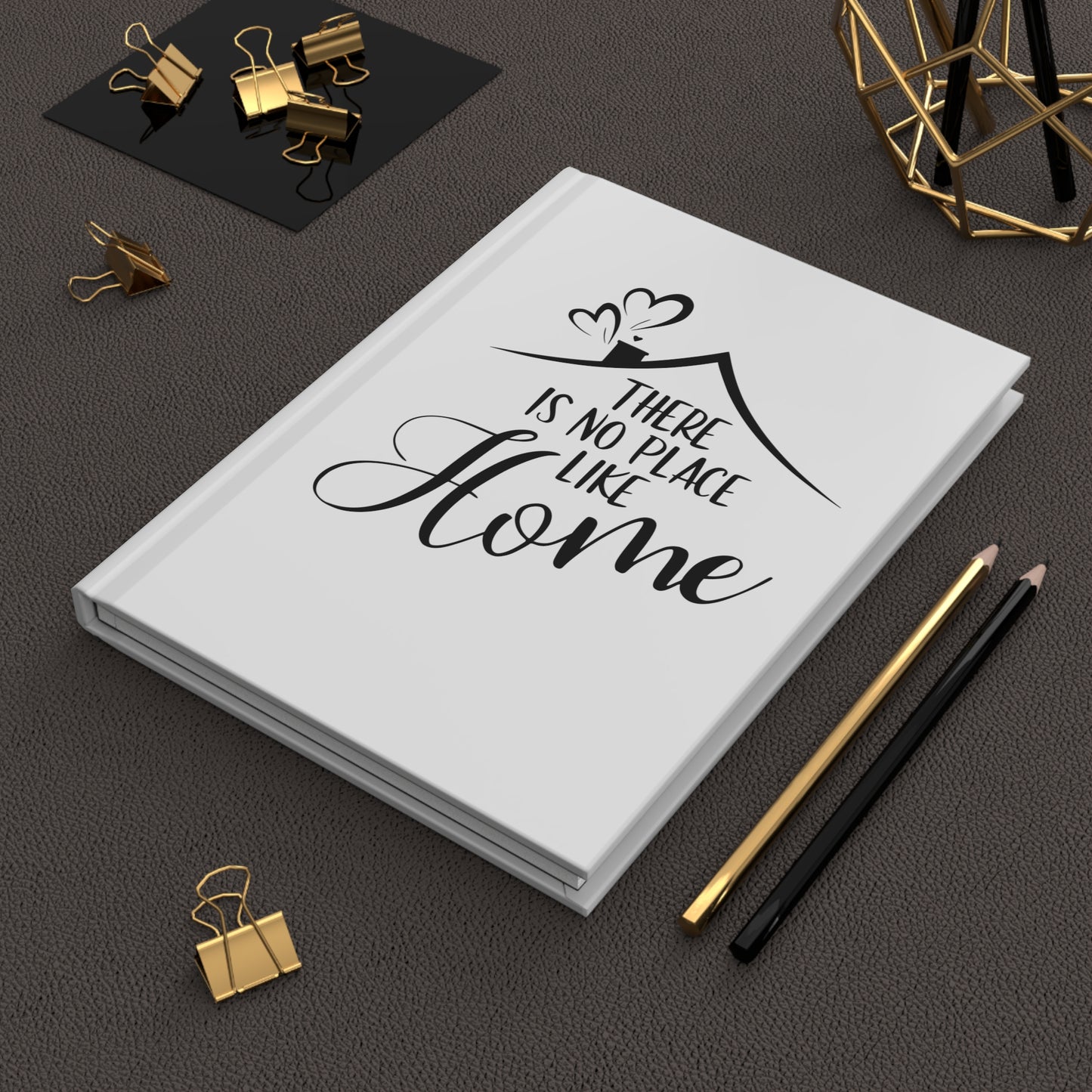 White hardcover journal with 'There is no place like home' quote on a dark surface with office supplies.