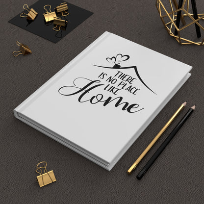 White hardcover journal with 'There is no place like home' quote on a dark surface with office supplies.