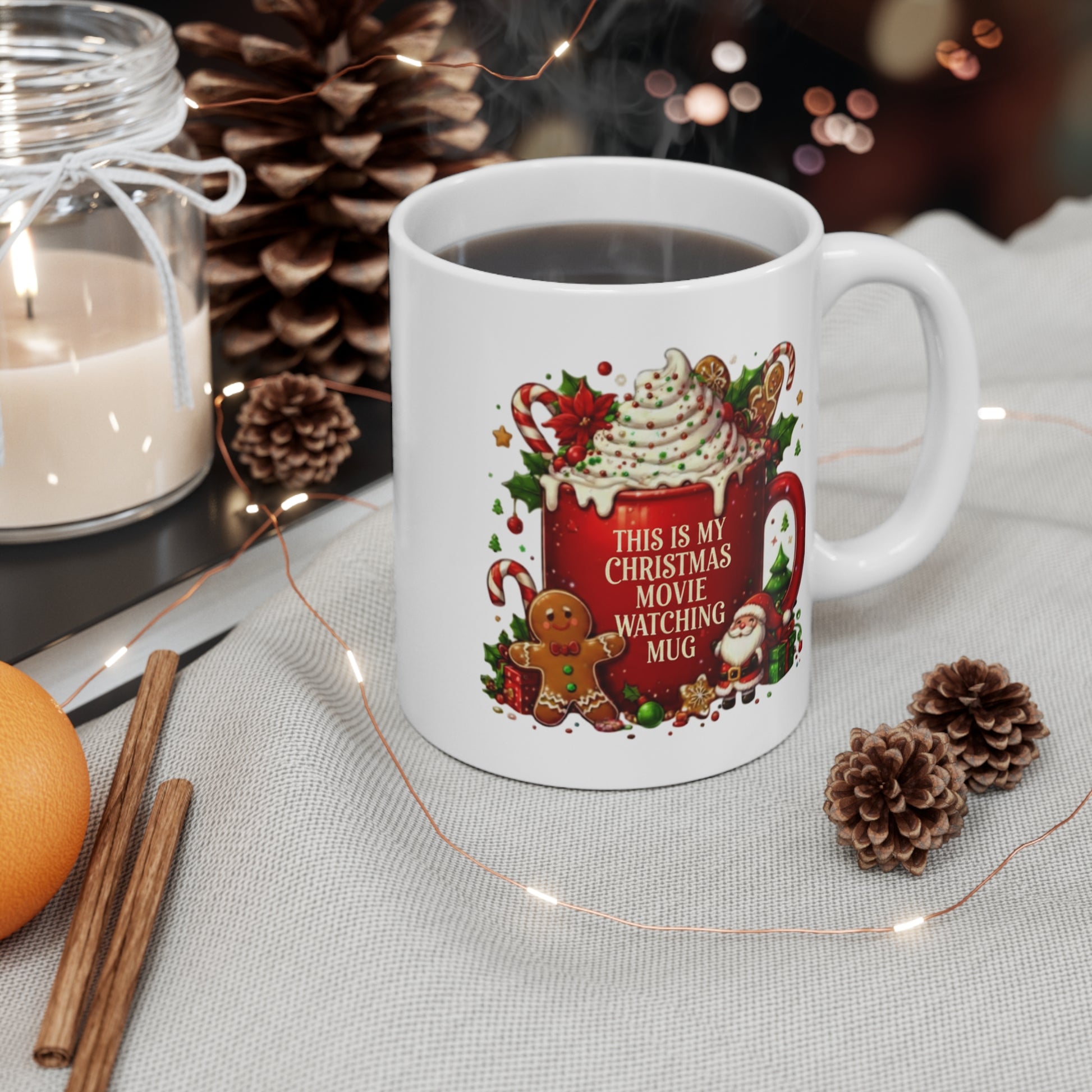 White ceramic mug with Christmas design and text "This Is My Christmas Movie Watching Mug", surrounded by decorative items on a table.