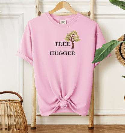 Tree Hugger T-shirt featuring a simple nature-inspired design with a brown and green tree graphic placed between the words Tree and Hugger in classic black font. Printed on a blossom pink unisex Comfort Colors tee, this eco-friendly design is perfect for environmentalists, outdoor lovers, hikers, and anyone passionate about protecting nature and forests.