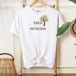 Tree Hugger T-shirt featuring a simple nature-inspired design with a brown and green tree graphic placed between the words Tree and Hugger in classic black font. Printed on a white unisex Comfort Colors tee, this eco-friendly design is perfect for environmentalists, outdoor lovers, hikers, and anyone passionate about protecting nature and forests.
