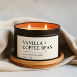 Vanilla and coffee bean soy wax blend candle in a black matte 8 oz candle tin on a wooden coaster with a beige cloth background