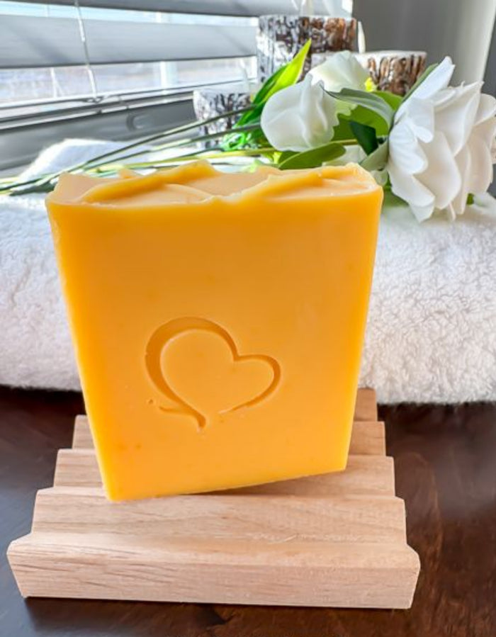 Citrus & Sage cold process soap with a heart imprint, handcrafted with an essential oil blend of orange, tangerine, lemon, pink grapefruit, sage, and cedarwood atlas. Vibrant golden-yellow bar displayed on a wooden soap dish, offering a refreshing, uplifting citrus aroma balanced with herbal and woody notes.