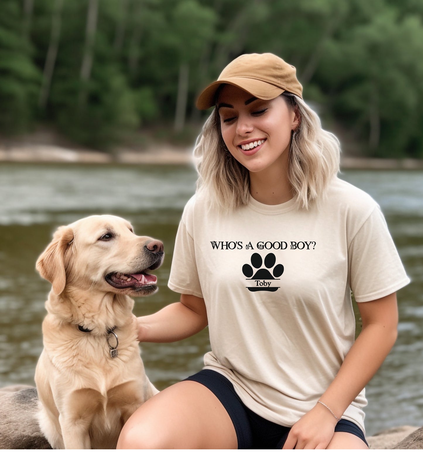 Woman wearing an Ivory t-shirt that reads “Who’s a Good Boy?” above a black paw print graphic with the name “Toby”.   Sitting with a golden retriever outdoors, the shirt is a playful and heartwarming tribute to a beloved pet—perfect for dog moms and puppy lovers.