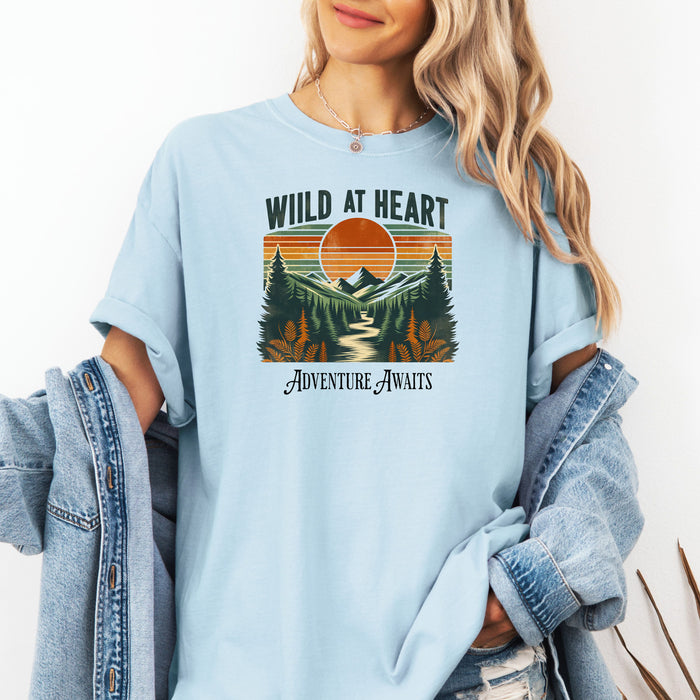 Vintage-style “Wild at Heart” graphic featuring a bold retro sunset over a pine forest and mountain scene, with a winding river flowing through the center. Warm earth tones—orange, green, and cream—create a nostalgic outdoor vibe. Ideal for adventure lovers and nature enthusiasts on a Comfort Colors Chambray (light blue) tee.