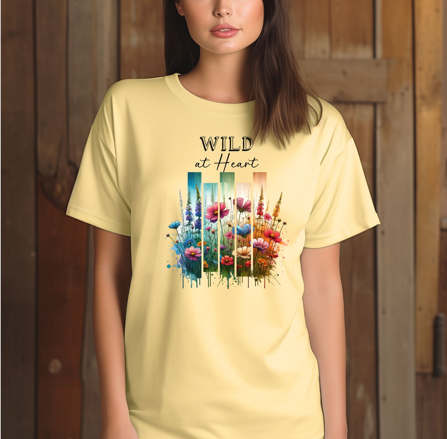 Banana “Wild at Heart” T-shirt featuring a vibrant watercolor-style design of wildflowers in pink, red, purple, yellow, and blue, set against vertical gradient bars in teal, green, and warm orange tones. The text “Wild at Heart” appears above the floral artwork in elegant black lettering. Perfect for nature lovers and free spirits, this casual tee offers a relaxed, stylish fit ideal for everyday wear.