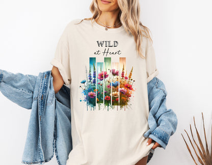 Ivory “Wild at Heart” T-shirt featuring a vibrant watercolor-style design of wildflowers in pink, red, purple, yellow, and blue, set against vertical gradient bars in teal, green, and warm orange tones. The text “Wild at Heart” appears above the floral artwork in elegant black lettering. Perfect for nature lovers and free spirits, this casual tee offers a relaxed, stylish fit ideal for everyday wear.