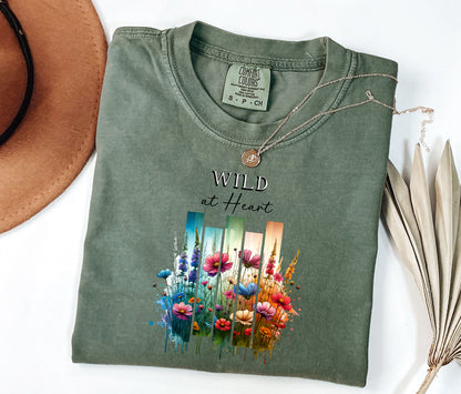 Moss “Wild at Heart” T-shirt featuring a vibrant watercolor-style design of wildflowers in pink, red, purple, yellow, and blue, set against vertical gradient bars in teal, green, and warm orange tones. The text “Wild at Heart” appears above the floral artwork in elegant black lettering. Perfect for nature lovers and free spirits, this casual tee offers a relaxed, stylish fit ideal for everyday wear.