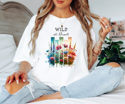 White “Wild at Heart” T-shirt featuring a vibrant watercolor-style design of wildflowers in pink, red, purple, yellow, and blue, set against vertical gradient bars in teal, green, and warm orange tones. The text “Wild at Heart” appears above the floral artwork in elegant black lettering. Perfect for nature lovers and free spirits, this casual tee offers a relaxed, stylish fit ideal for everyday wear.