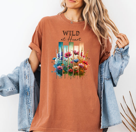 Yam “Wild at Heart” T-shirt featuring a vibrant watercolor-style design of wildflowers in pink, red, purple, yellow, and blue, set against vertical gradient bars in teal, green, and warm orange tones. The text “Wild at Heart” appears above the floral artwork in elegant black lettering. Perfect for nature lovers and free spirits, this casual tee offers a relaxed, stylish fit ideal for everyday wear.