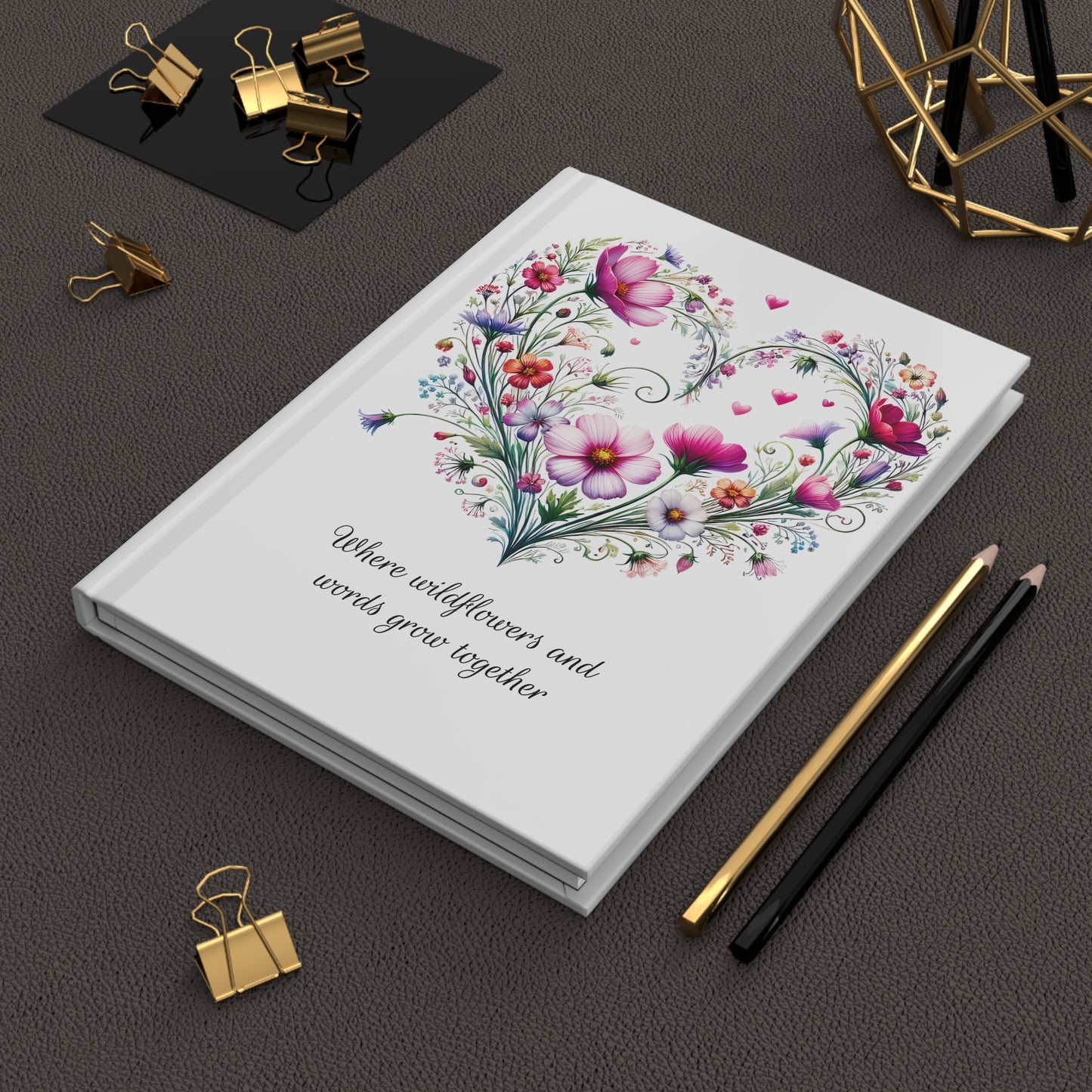 Hardcover journal with floral design and text on a dark surface with stationery items.