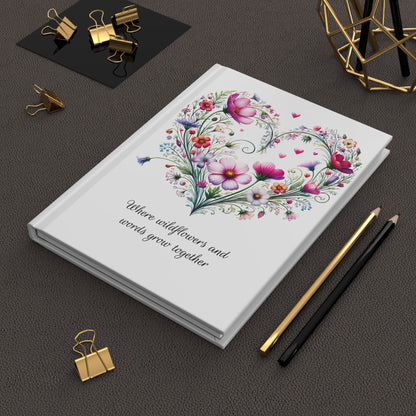 Hardcover journal with floral design and text on a dark surface with stationery items.