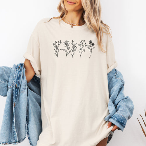 Ivory Comfort Colors® t-shirt featuring a minimalist white line art wildflower design across the chest. Simple hand-drawn botanical outlines create a delicate and nature-inspired look, perfect for plant lovers, gardeners, and boho style. Soft, relaxed fit ideal for casual everyday wear.