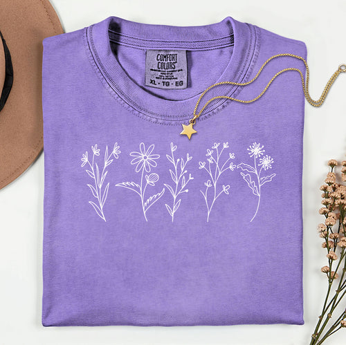 Violet Comfort Colors® t-shirt featuring a minimalist white line art wildflower design across the chest. Simple hand-drawn botanical outlines create a delicate and nature-inspired look, perfect for plant lovers, gardeners, and boho style. Soft, relaxed fit ideal for casual everyday wear.
