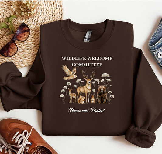 Dark Chocolate Gildan sweatshirt featuring a heartwarming “Wildlife Welcome Committee” design with detailed illustrations of woodland animals—deer, bear, owl, fox, rabbit, and more—surrounded by wildflowers. The phrase “Honor and Protect” appears below, promoting love and respect for nature. Perfect for wildlife enthusiasts and outdoor lovers.