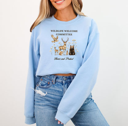Light Blue Gildan sweatshirt featuring a heartwarming “Wildlife Welcome Committee” design with detailed illustrations of woodland animals—deer, bear, owl, fox, rabbit, and more—surrounded by wildflowers. The phrase “Honor and Protect” appears below, promoting love and respect for nature. Perfect for wildlife enthusiasts and outdoor lovers.
