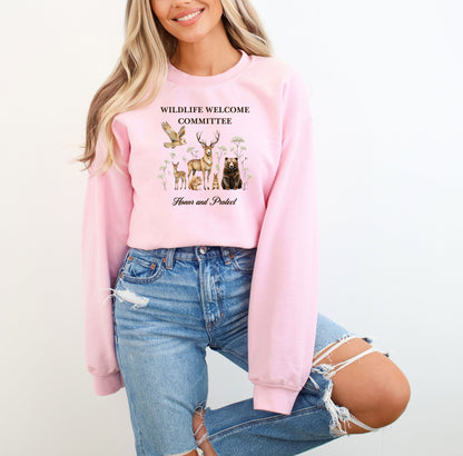 Light Pink Gildan sweatshirt featuring a heartwarming “Wildlife Welcome Committee” design with detailed illustrations of woodland animals—deer, bear, owl, fox, rabbit, and more—surrounded by wildflowers. The phrase “Honor and Protect” appears below, promoting love and respect for nature. Perfect for wildlife enthusiasts and outdoor lovers.