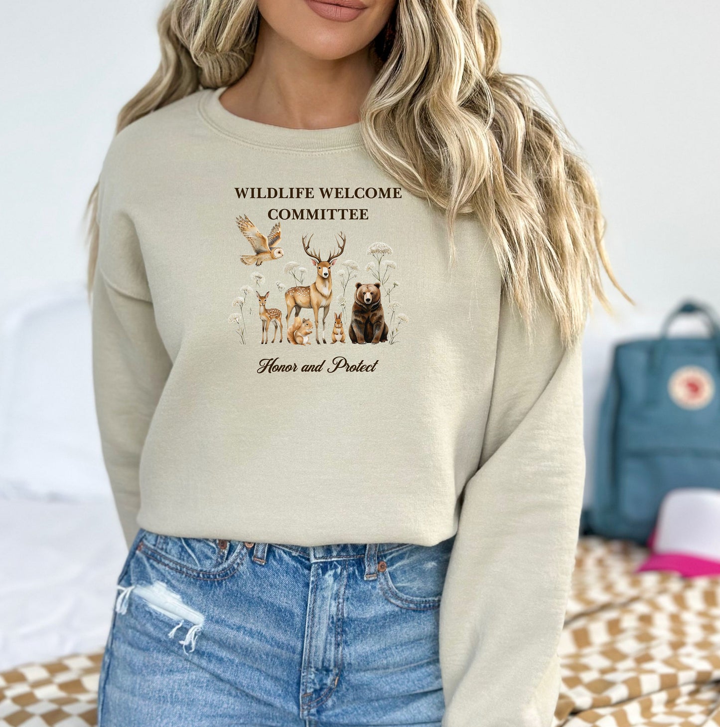 Sand Gildan sweatshirt featuring a heartwarming “Wildlife Welcome Committee” design with detailed illustrations of woodland animals—deer, bear, owl, fox, rabbit, and more—surrounded by wildflowers. The phrase “Honor and Protect” appears below, promoting love and respect for nature. Perfect for wildlife enthusiasts and outdoor lovers.