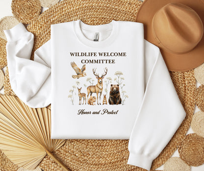 White Gildan sweatshirt featuring a heartwarming “Wildlife Welcome Committee” design with detailed illustrations of woodland animals—deer, bear, owl, fox, rabbit, and more—surrounded by wildflowers. The phrase “Honor and Protect” appears below, promoting love and respect for nature. Perfect for wildlife enthusiasts and outdoor lovers.