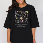 A woman standing wearing the black t-shirt.  The text reads 'you belong among the Wildflowers'.  Above the text shows a grid of wildflowers.