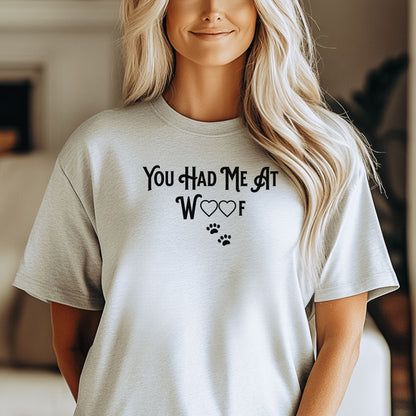Person wearing an ash T-shirts featuring the phrase “You Had Me At Woof” in playful black text. The design includes heart shapes inside the letters and two small paw prints beneath, creating a cute and stylish look perfect for dog lovers and pet owners.