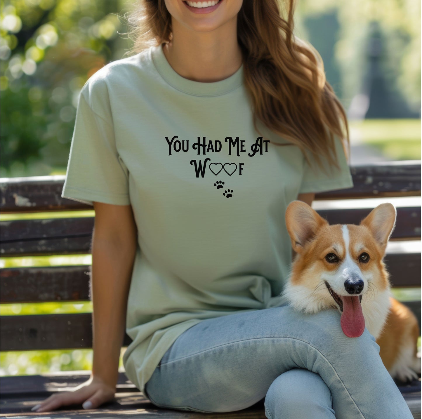 Person wearing a sage T-shirts featuring the phrase “You Had Me At Woof” in playful black text. The design includes heart shapes inside the letters and two small paw prints beneath, creating a cute and stylish look perfect for dog lovers and pet owners.