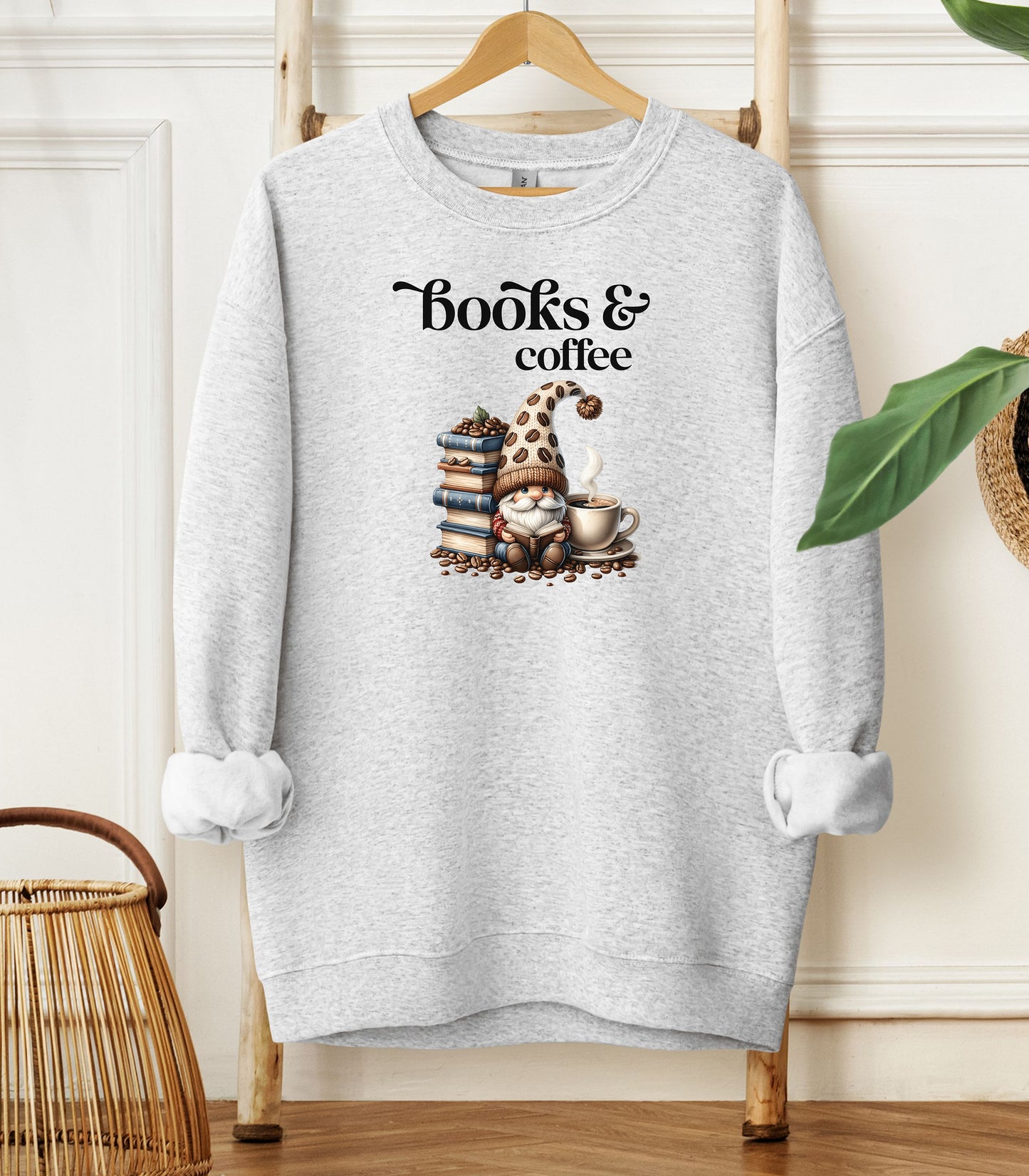 Ash Gildan sweatshirt featuring an adorable “Books & Coffee” design with a cozy gnome wearing a polka-dot hat, sitting beside a stack of books, a steaming coffee cup, and scattered coffee beans. A charming and whimsical design perfect for book lovers, coffee enthusiasts, and fall vibes.