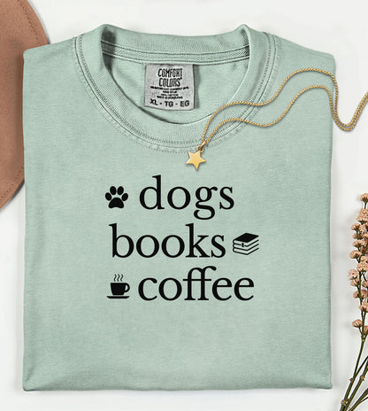 Black graphic design on a bay t-shirt featuring the phrase “Dogs, Books, Coffee” in bold, playful lettering. Decorative icons of a dog paw, stacked books, and a steaming coffee cup enhance the cozy, laid-back vibe—perfect for dog lovers, bookworms, and caffeine enthusiasts alike.