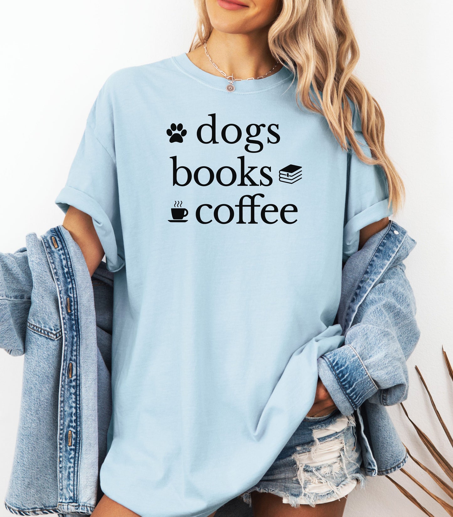 Black graphic design on a Chambray light blue t-shirt featuring the phrase “Dogs, Books, Coffee” in bold, playful lettering. Decorative icons of a dog paw, stacked books, and a steaming coffee cup enhance the cozy, laid-back vibe—perfect for dog lovers, bookworms, and caffeine enthusiasts alike.