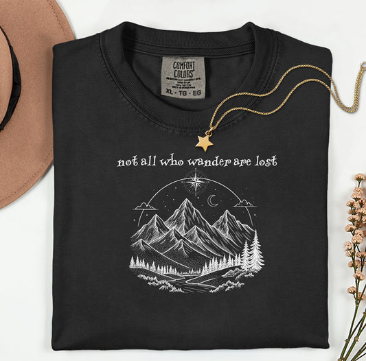 Not All Who Wander Are Lost T-shirt featuring an artistic nature scene with hand-drawn mountains, pine trees, a winding trail, and a starry sky with a crescent moon. This adventurous design, printed on a soft, black comfortable unisex tee, inspires exploration, travel, and a free-spirited lifestyle. Perfect for hikers, nature lovers, and wanderers who embrace the journey and find peace in the great outdoors.