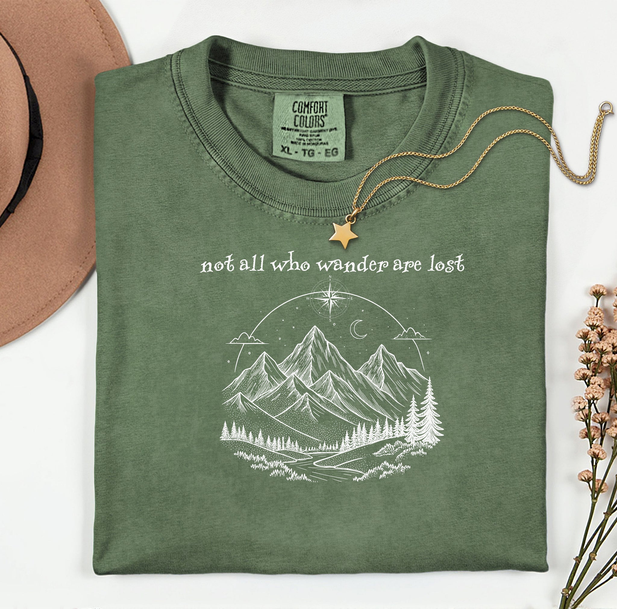 Not All Who Wander Are Lost T-shirt featuring an artistic nature scene with hand-drawn mountains, pine trees, a winding trail, and a starry sky with a crescent moon. This adventurous design, printed on a soft, hemp color comfortable unisex tee, inspires exploration, travel, and a free-spirited lifestyle. Perfect for hikers, nature lovers, and wanderers who embrace the journey and find peace in the great outdoors.