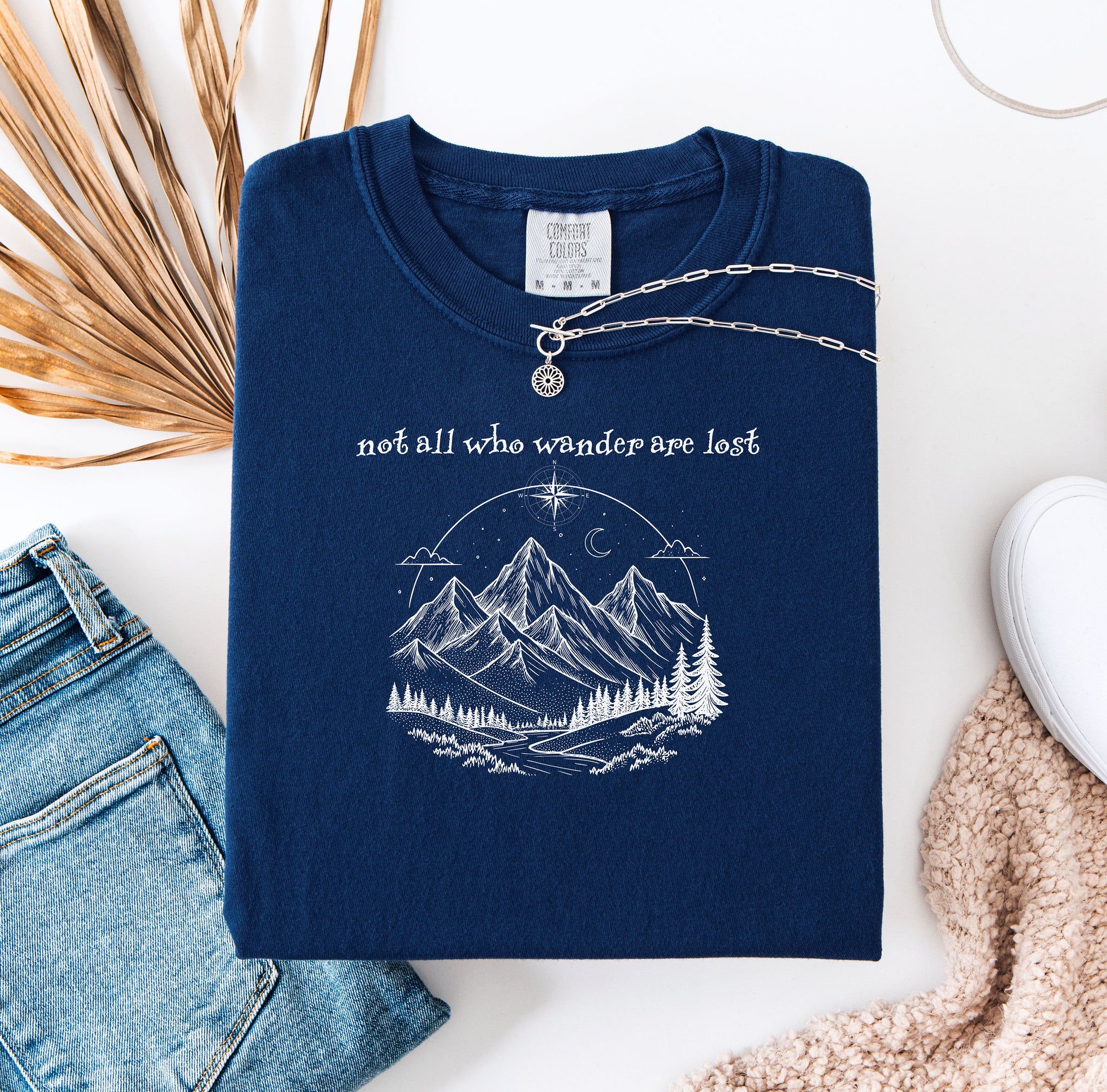 Not All Who Wander Are Lost T-shirt featuring an artistic nature scene with hand-drawn mountains, pine trees, a winding trail, and a starry sky with a crescent moon. This adventurous design, printed on a soft, true navy comfortable unisex tee, inspires exploration, travel, and a free-spirited lifestyle. Perfect for hikers, nature lovers, and wanderers who embrace the journey and find peace in the great outdoors.